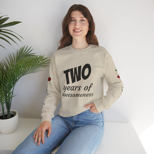 Person wearing a beige sweatshirt with 'TWO years of awesomeness' text, sitting on a white surface with a plant in the background.
