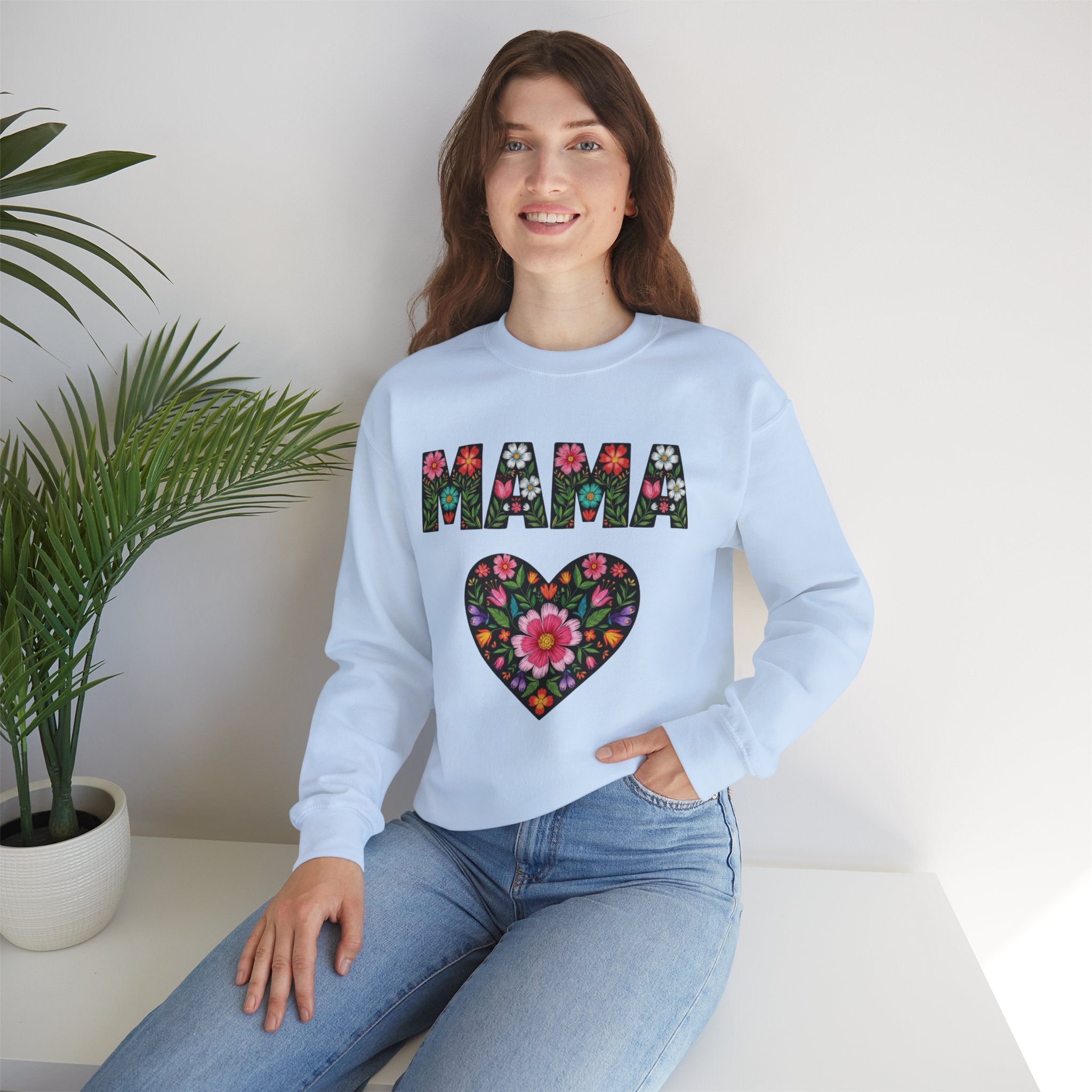 Woman wearing a light blue sweatshirt with floral 'MAMA' design sitting on a white surface.