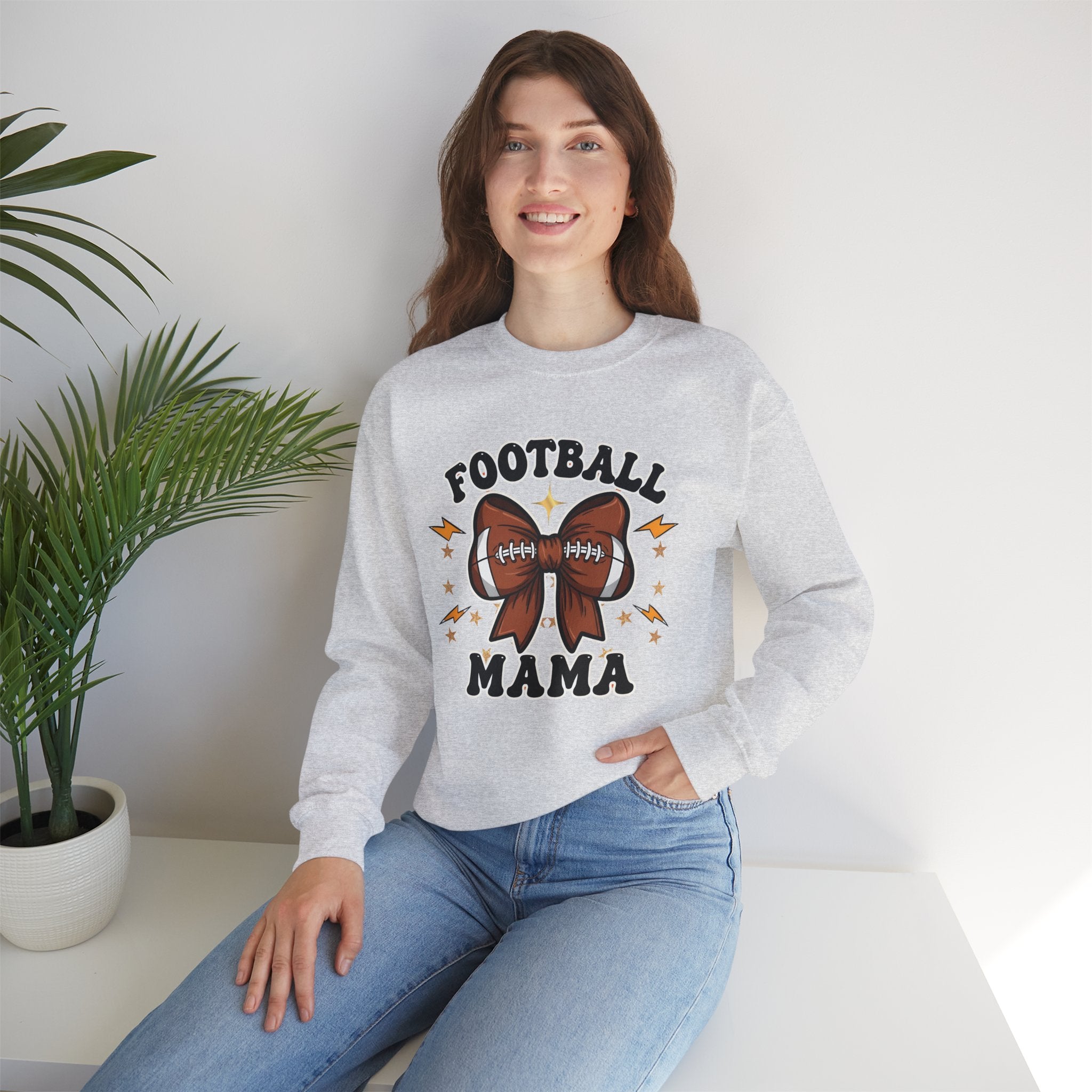 Woman wearing a gray sweatshirt with 'Football Mama' text and graphics, sitting in a room with a plant.