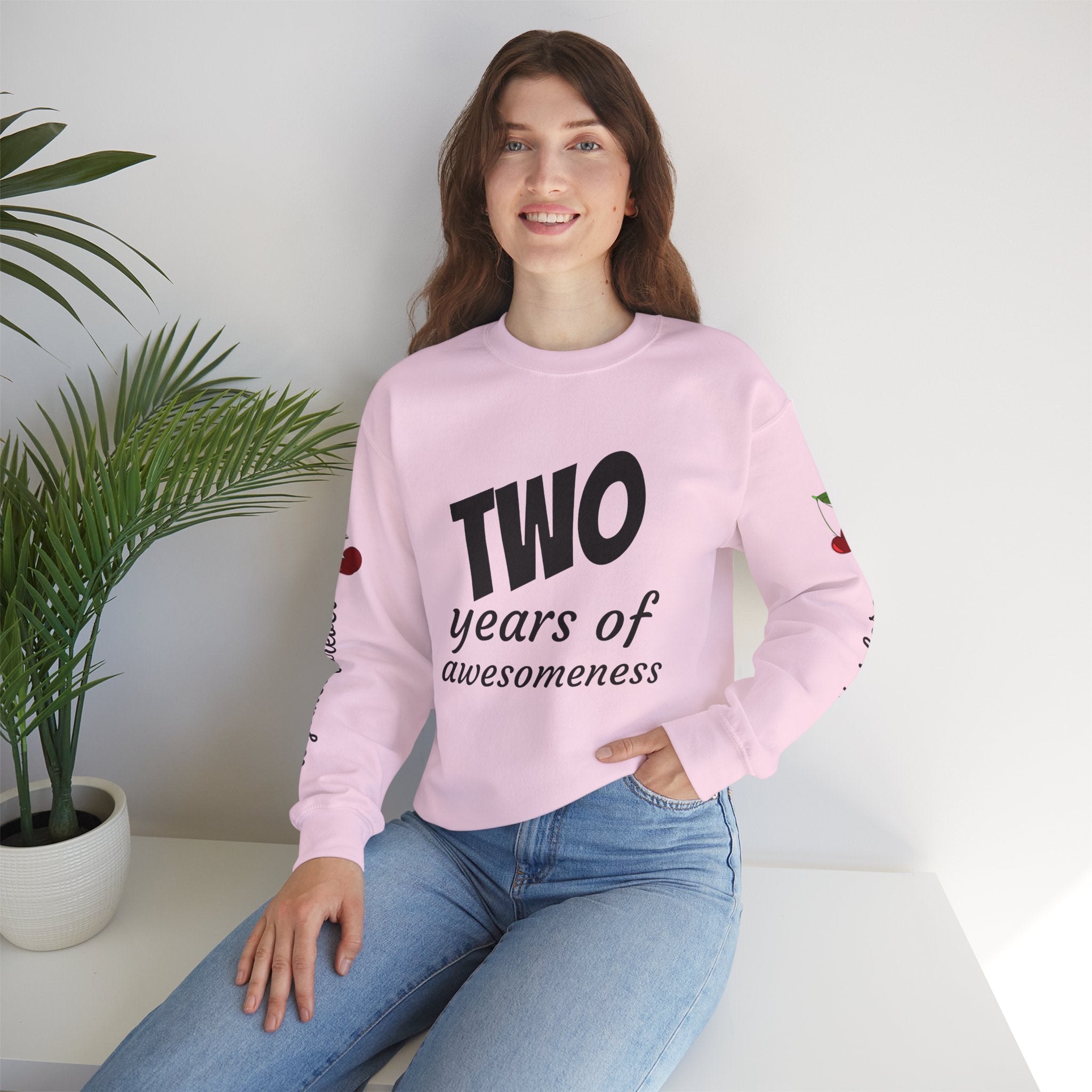 Person wearing a pink sweatshirt with text, sitting on a white surface with a plant in the background