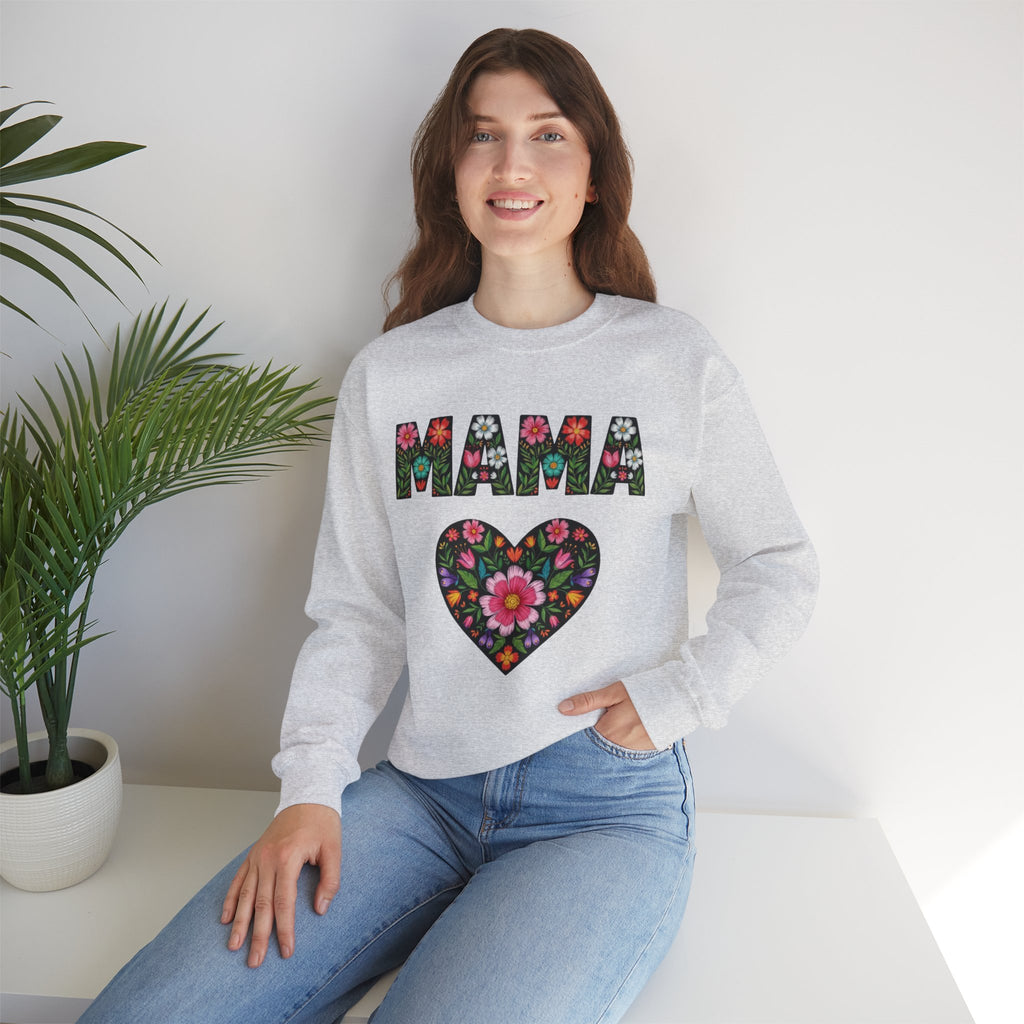 Woman wearing a gray sweatshirt with floral 'MAMA' design sitting on a white surface with a plant in the background.