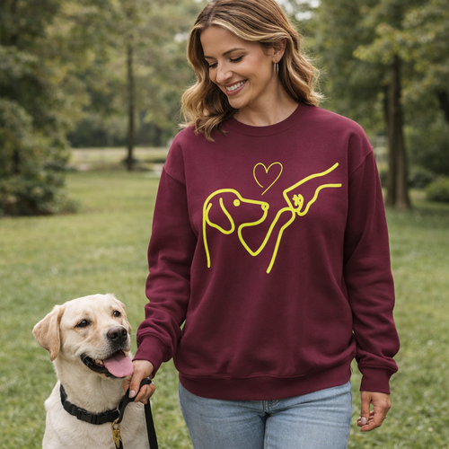 Woman wearing a maroon sweatshirt with a yellow dog design, standing outdoors with a dog.