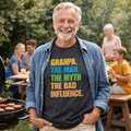 Man wearing a t-shirt with colorful text standing outdoors near a grill.